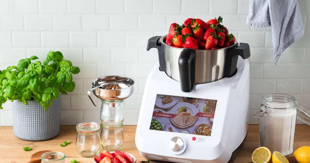 Der Monsieur Cuisine auf einer Arbeitsplatte aus Holz, im Mixbehälter sind Erdbeeren, die über den Rand schauen