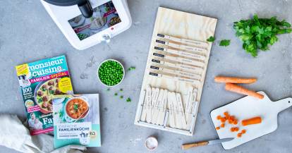 Auf einer Arbeitsplatte liegen ein Speiseplan, ein Familien-Kochbuch, das neue Familien-Spezial, der Monsieur Cuisine sowie einige frische Lebensmittel