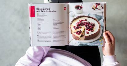 Jemand hält das aufgeschlagene Monsieur Cuisine Basis-Kochbuch in den Händen.