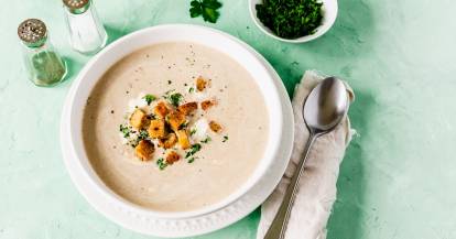 Ein weißer Teller mit heller Suppe auf grünem Untergrund