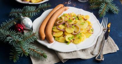 Weißer Teller mit Kartoffelsalat und zwei Würstchen in weihnachtlicher Deko