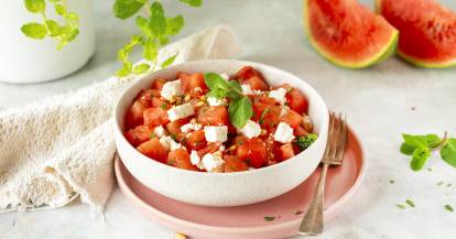 Wassermelone und Feta Salat in einer hellen Schüssel, daneben ein Tuch und Melone