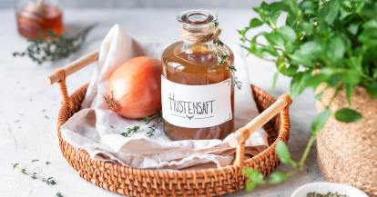 Eine Flasche Hustensaft und eine Zwiebel, daneben Kräuter