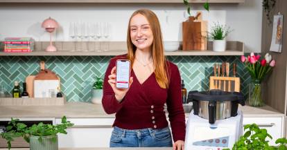 Isy von ZauberMix mit ihrem Telefon und dem Warenkorb von REWE auf dem Bildschirm