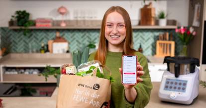 Isy von ZauberMix mit einer Tüte voller Lebensmittel von REWE und ihrem Smartphone