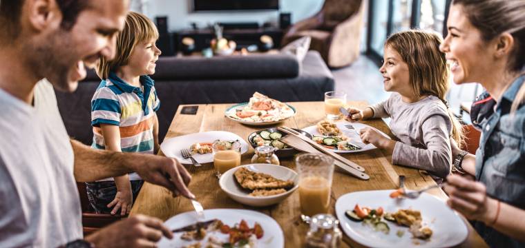 Vierköpfige Familie sitzt am gedeckten Esstisch und unterhält sich