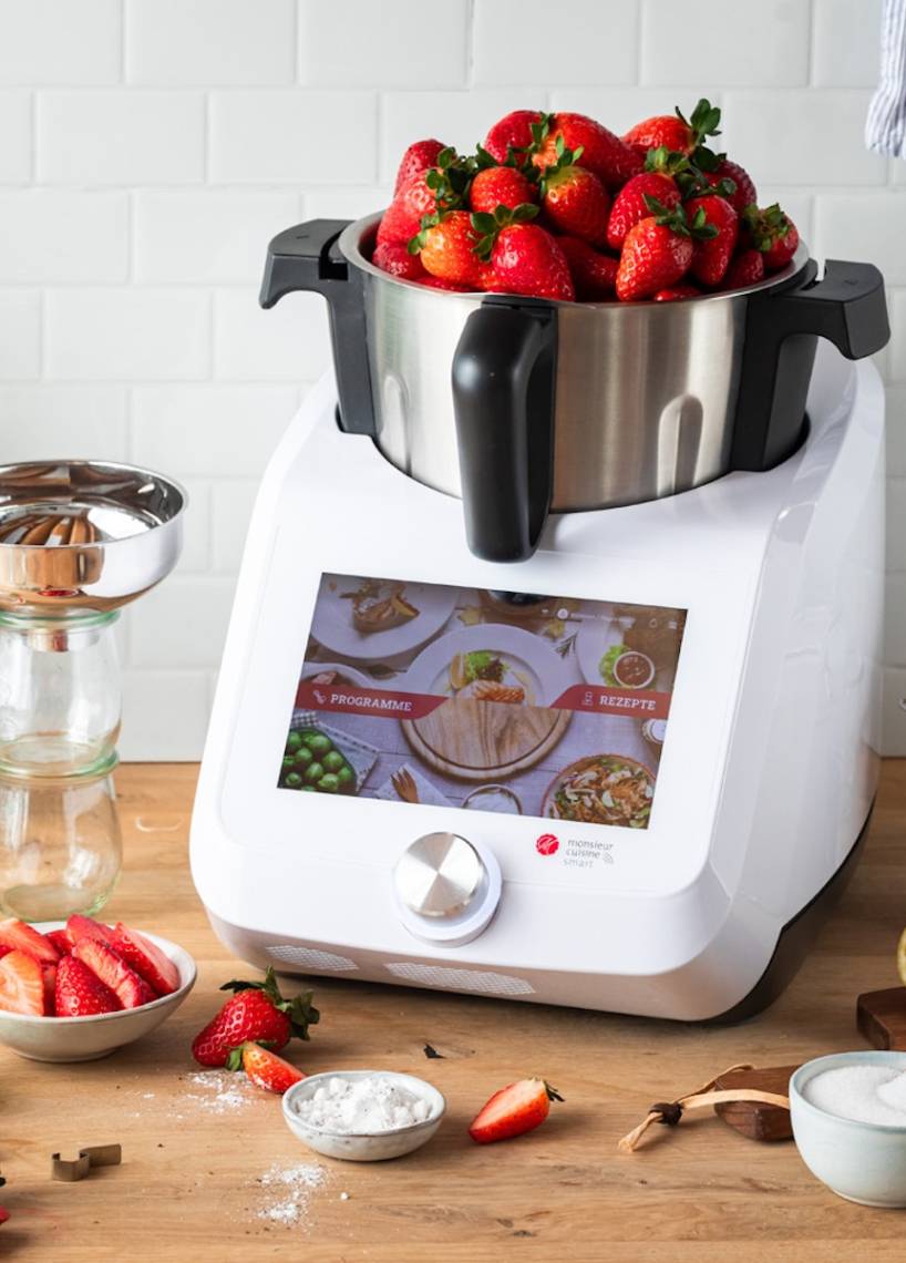 Der Monsieur Cuisine auf einer Arbeitsplatte aus Holz, im Mixbehälter sind Erdbeeren, die über den Rand schauen